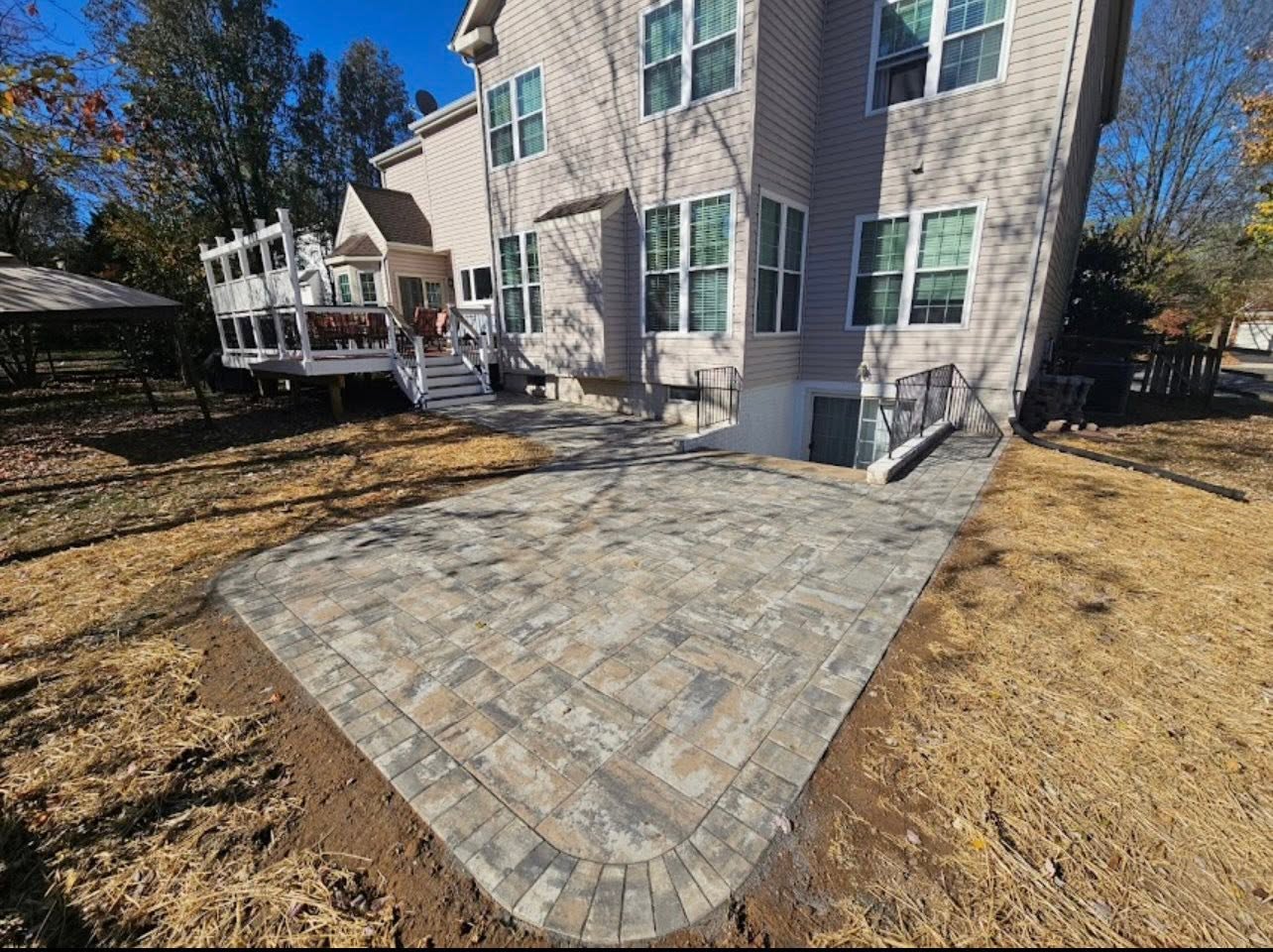 Paver patio with a fire-pit seating area set into a backyard